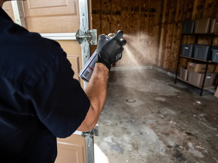 A technician sprays lubricant on a garage door hinge.